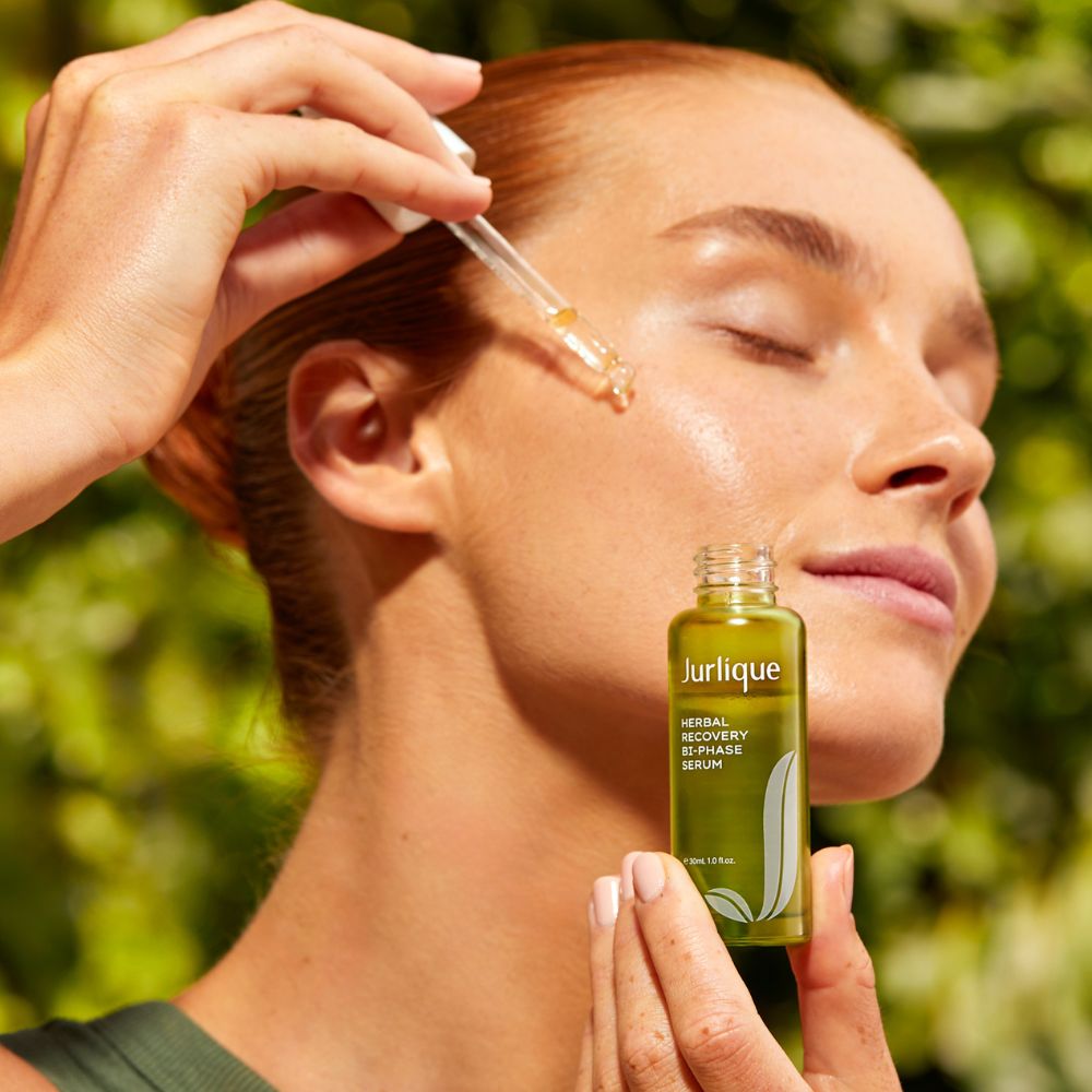Woman applying Jurlique serum to her face with a dropper, greenery in the background