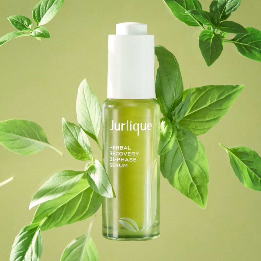 Jurlique Herbal Recovery Two-Phase Serum bottle surrounded by green leaves on a light green background