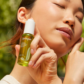 Woman holding a Jurlique skincare serum bottle with a blurred green background