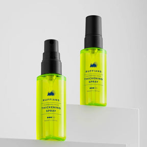 Two bottles of Ruffians Thickening Spray in translucent neon yellow-green with black spray tops, displayed on a clean white geometric surface against a light gray background.